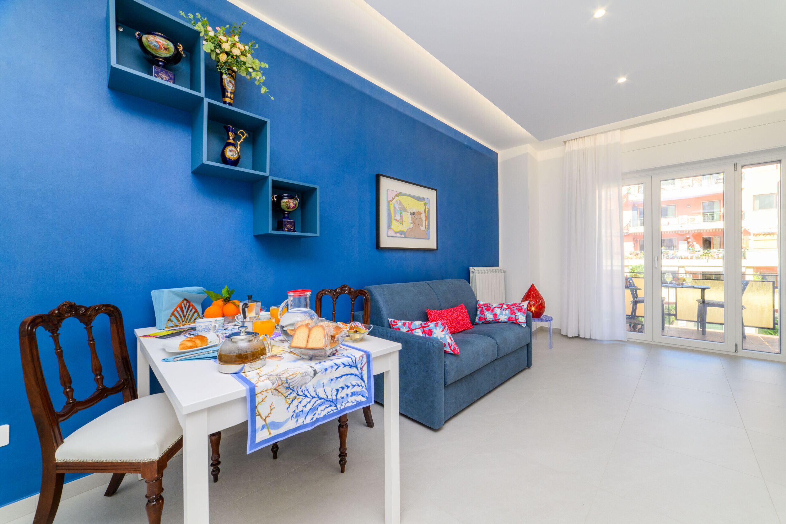 A dining area with a table set for breakfast, a blue sofa, and a view of the outside.