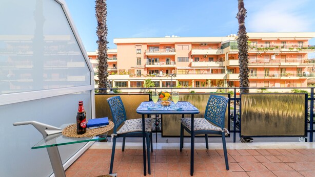 Ein Balkon mit Tisch, Stühlen, einer Flasche und Blick auf ein mehrstöckiges Gebäude.