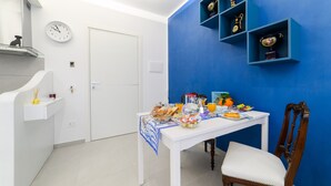 Eine Küche mit einem weißen Esstisch, der für das Frühstück gedeckt ist, einer Uhr an der Wand und blauen Regalen mit dekorativen Gegenständen.