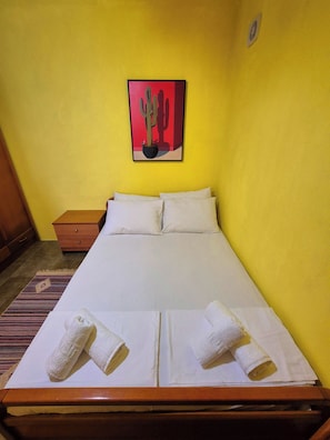 Un letto con lenzuola e asciugamani bianchi, una testiera in legno, un comodino e un quadro raffigurante un cactus al muro.
