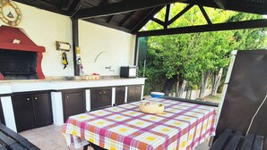An outdoor kitchen area with a grill, a sink, and a table covered with a checkered tablecloth. - GeoBasement - Mexico (Pefkochori)