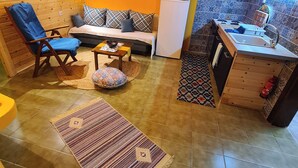 A compact living space with a sofa, a chair, a small table, a refrigerator, a sink, and a patterned rug. - GeoBasement - Mexico (Pefkochori)