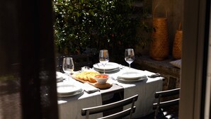 Mesa de comedor al aire libre dispuesta con platos, vasos y un bol de tomates.