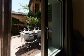 An outdoor dining area with a table set for two, a chair, and a window with a view of a building and greenery. - Casetta Monti (Brunate)