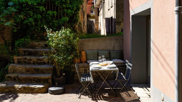 Un pequeño espacio de comedor al aire libre con una mesa preparada para dos personas, rodeado de escalones de piedra y vegetación.
