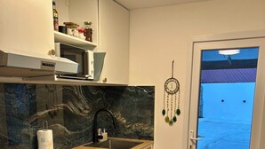 A kitchen with a black stove, a sink, and a wooden countertop. There is a dreamcatcher on the wall and a door leading outside.
