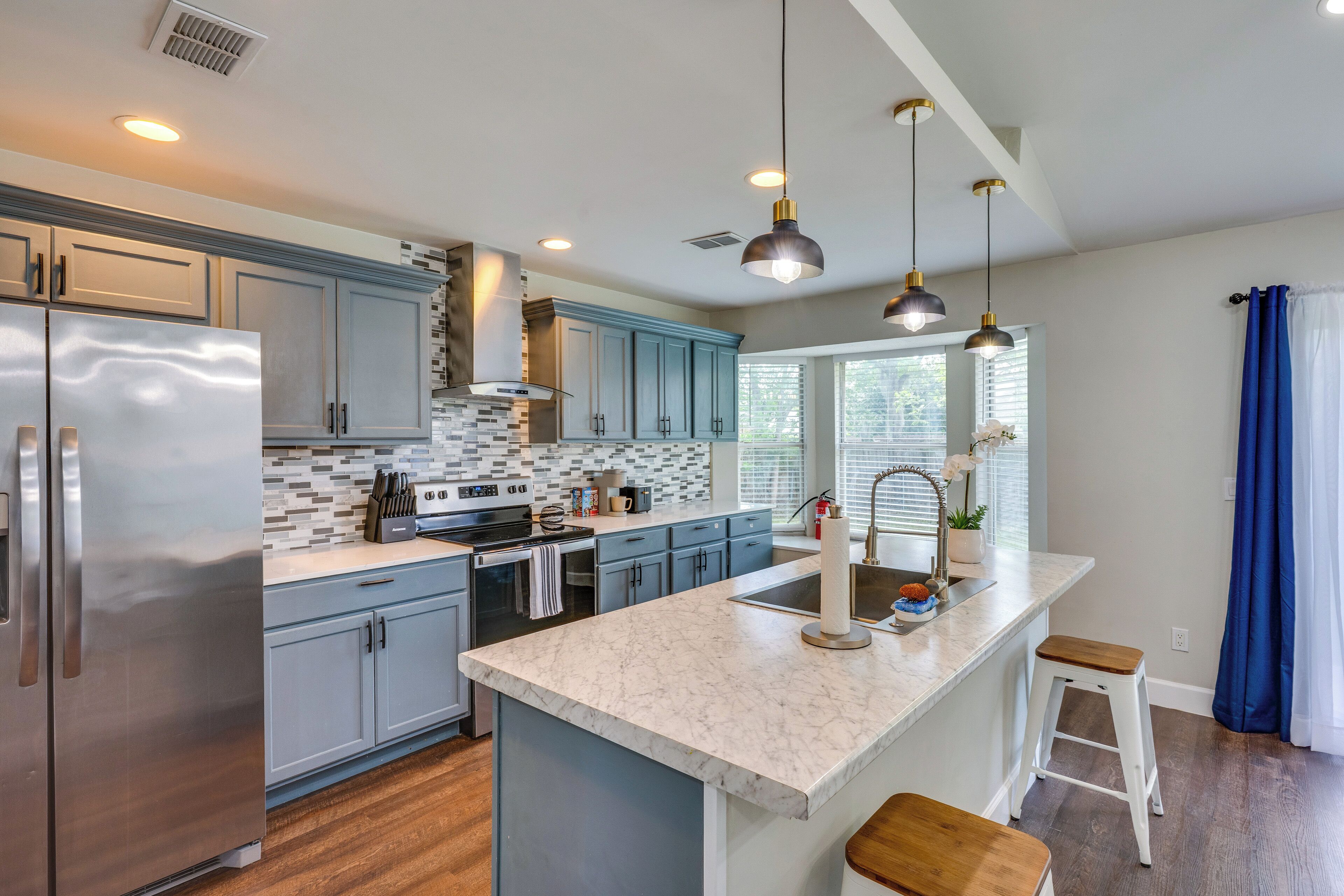 A modern kitchen with a stainless steel refrigerator, a marble countertop island, and pendant lighting.