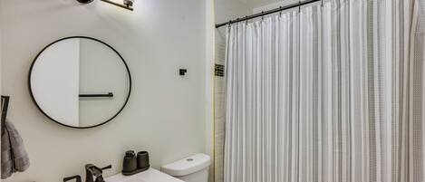 A bathroom with a round mirror, a white sink, a toilet, and a shower curtain.