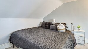 Een slaapkamer met een bed, kussens, een bedlampje, een nachtkastje en een kleine plant.