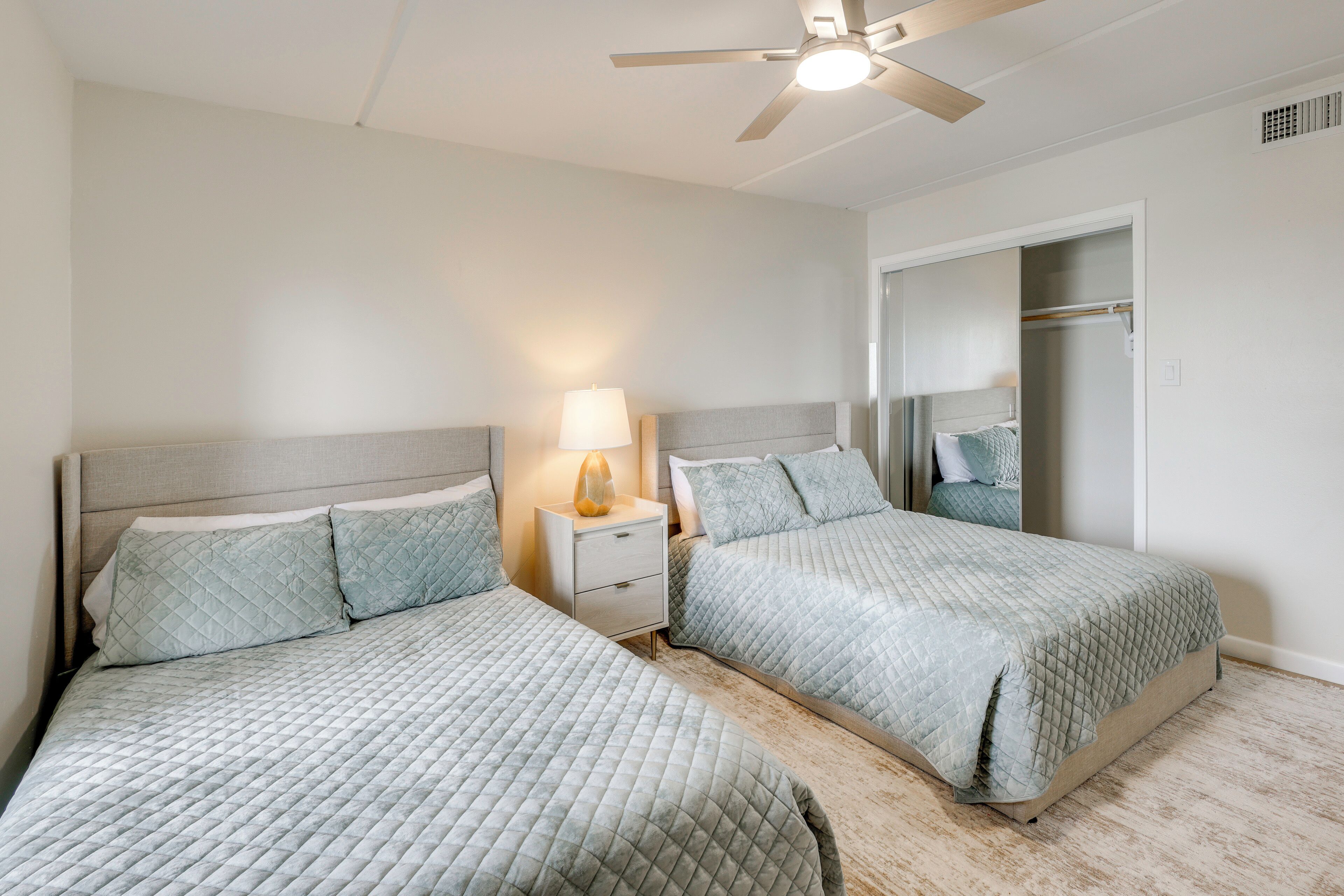 A bedroom with two beds, a nightstand with a lamp, a ceiling fan, and a walk-in closet.