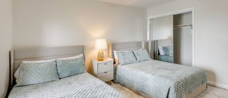 A bedroom with two beds, a nightstand with a lamp, a ceiling fan, and a walk-in closet.