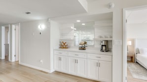 A modern kitchen with white cabinetry, a large mirror, and a coffee machine. - Stunning Views, Luxe Decor: Suntide III - Unit 805 (South Padre Island)