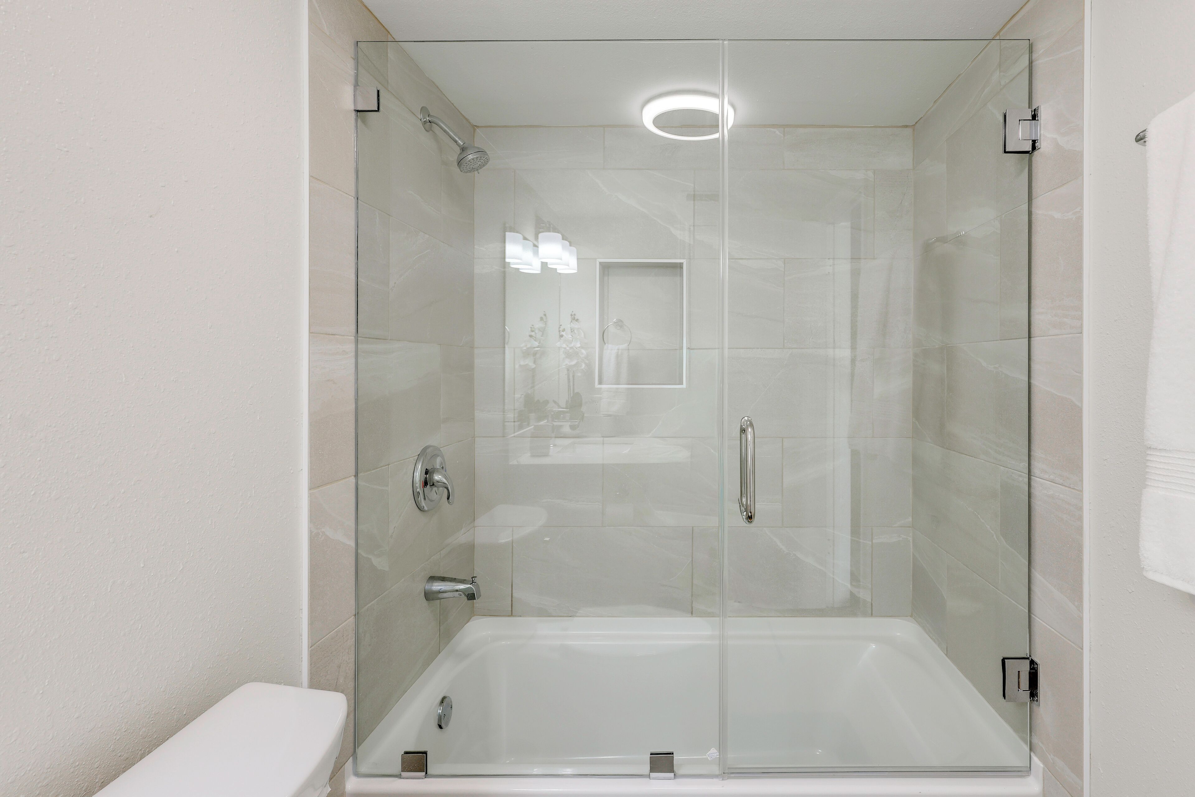 Et moderne badeværelse med et glasafskærmet brusebad, et hvidt toilet og et synligt håndklædestativ.