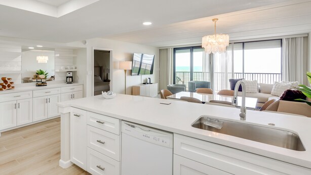 A modern kitchen with a dishwasher, a dining area with a table and chairs, and a view of the ocean through large windows. - Stunning Views, Luxe Decor: Suntide III - Unit 805 (South Padre Island)