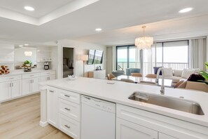 A modern kitchen with a dishwasher, a dining area with a table and chairs, and a view of the ocean through large windows. - Stunning Views, Luxe Decor: Suntide III - Unit 805 (South Padre Island)