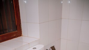 A white toilet with a tank, a bidet, and a toilet paper holder in a bathroom with white tiled walls and floor. - The Hub Train House Exotic Roots (Zanzibar Town)