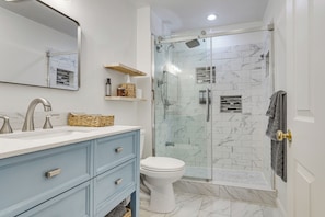 A bathroom with a glass-enclosed shower, a white toilet, a vanity with drawers, and a mirror.