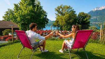 Deux personnes sont assises sur des chaises de jardin rouges, face à face, et profitent d’une vue magnifique sur les montagnes et un lac en arrière-plan.