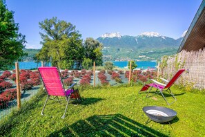 Ein Garten mit zwei roten Stühlen und einer Feuerstelle, mit Blick auf eine Berglandschaft und ein Gewässer.