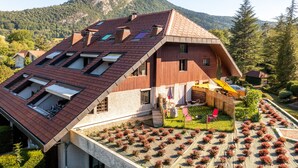 Una casa moderna con techo inclinado, varios tragaluces y un jardín con plantas en macetas.