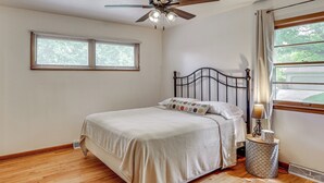 Un dormitorio con cama, ventilador de techo, ventana con persianas y lámpara de noche.