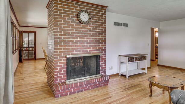 Una sala de estar con chimenea de ladrillo, suelo de madera y mueble de entretenimiento blanco.