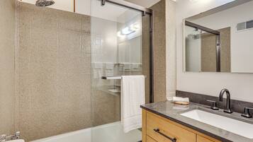 A modern bathroom with a glass-enclosed shower, a white sink, and a large mirror.