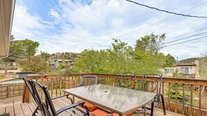 Eine Holzdielen-Terrasse mit einem Glastisch und Metallstühlen, mit Blick auf ein Wohngebiet mit Häusern und Bäumen.