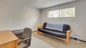 Ein Zimmer mit Holzschreibtisch, schwarzem Ledersofa, einem kleinen Tisch, einem Stuhl, einem Fenster mit Jalousien und einer Deckenleuchte.
