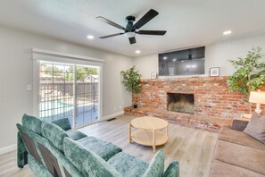 A living room with a brick fireplace, a ceiling fan, and a sliding glass door leading to a balcony. - Near Fresno State & Malls! Family-friendly Home (Fresno)