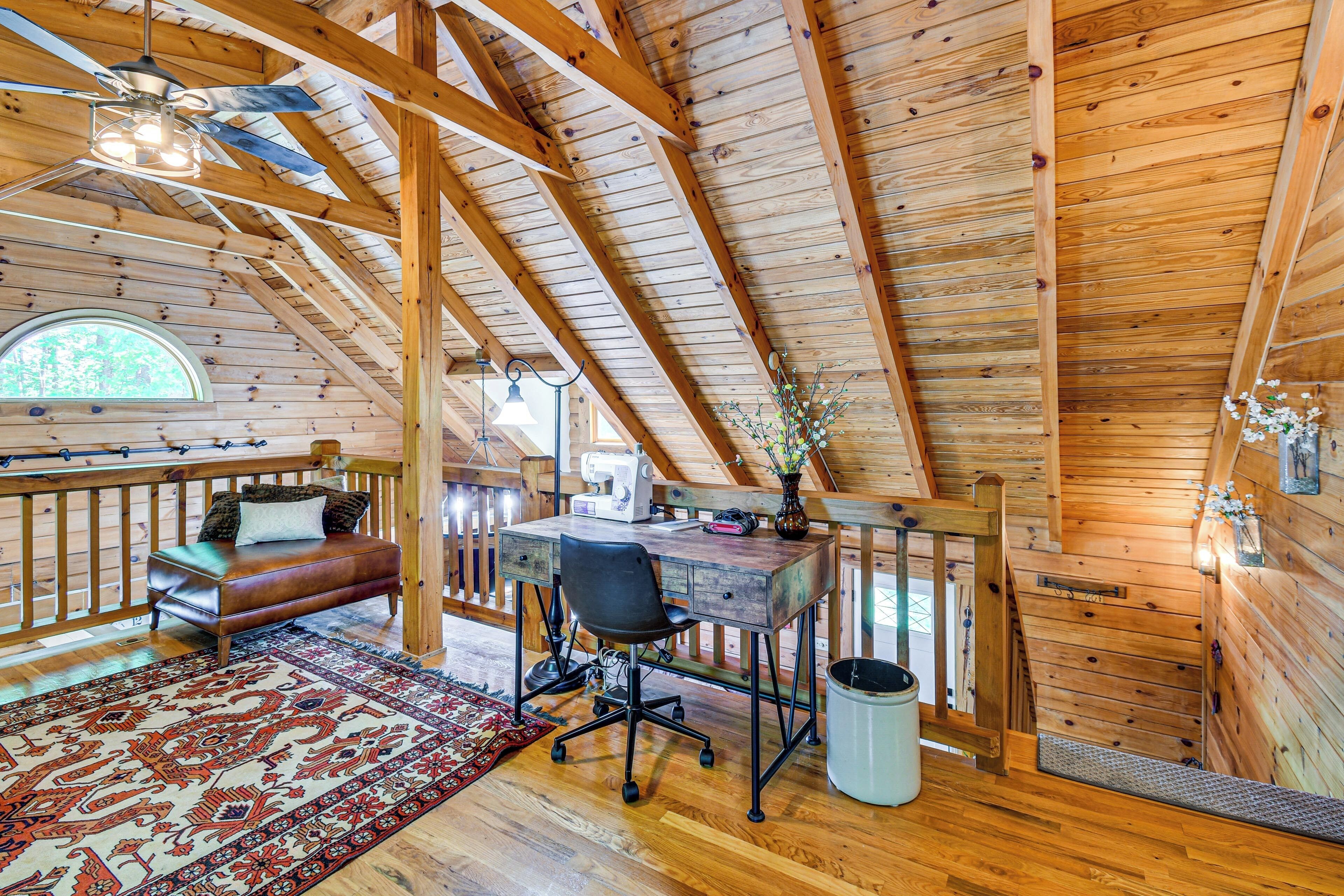A loft bedroom with a wooden ceiling, a desk, a chair, a bed, a window, and a view of the outdoors.