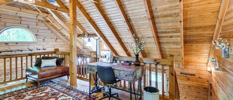A loft bedroom with a wooden ceiling, a desk, a chair, a bed, a window, and a view of the outdoors.