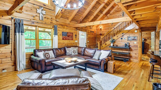 A wooden cabin interior with a leather sectional sofa, a dining table, and a staircase. - Hot Tub & Patio: Bedford Log Cabin on 10 Acres! (Moneta)