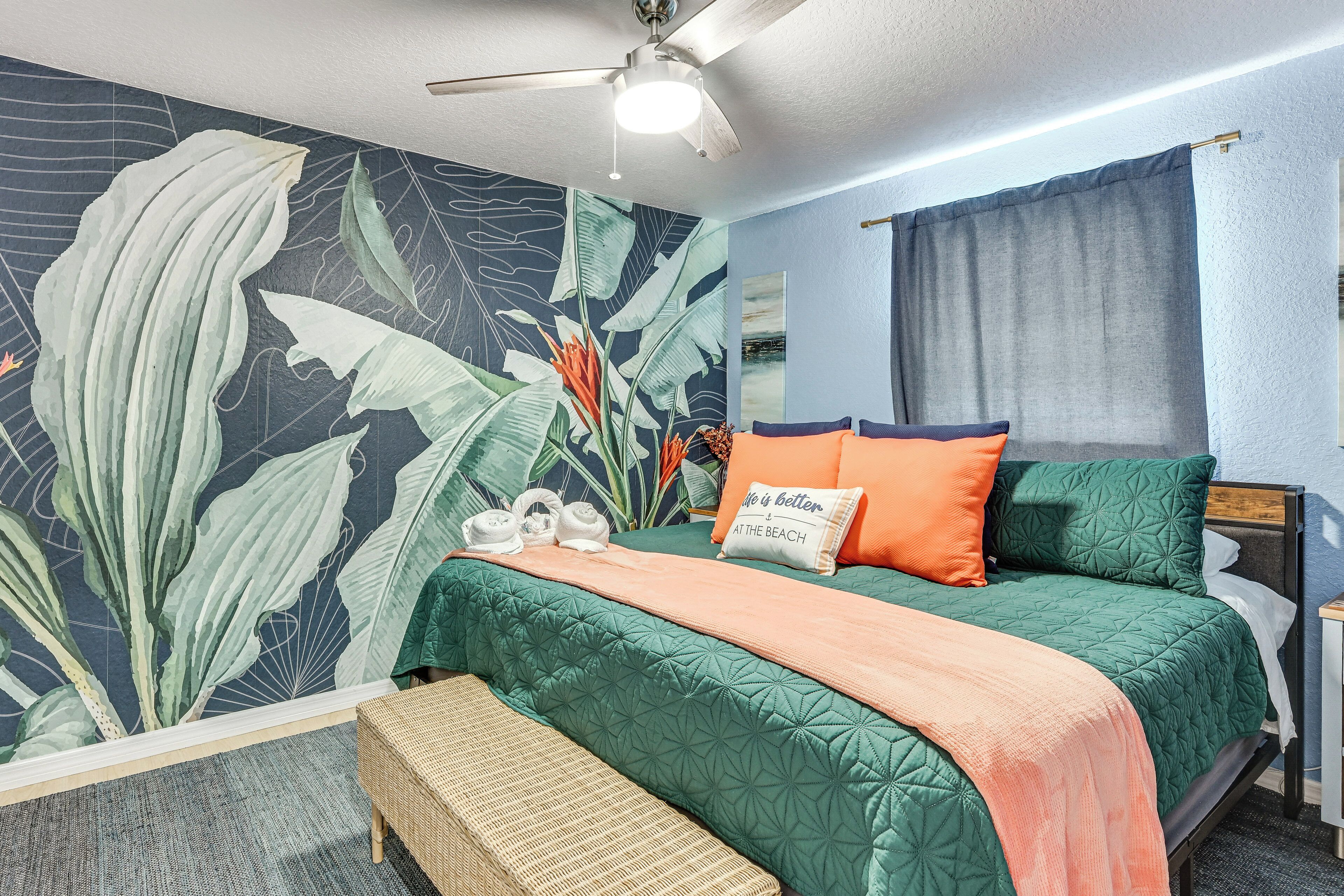 A bedroom with a bed, a ceiling fan, a wall mural, and a bench.