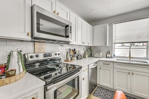 Una cocina con armarios blancos, microondas de acero inoxidable, horno doble y lavavajillas.