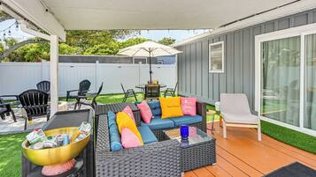 Une terrasse couverte, aménagée avec du mobilier d’extérieur, un barbecue et un grand parasol.