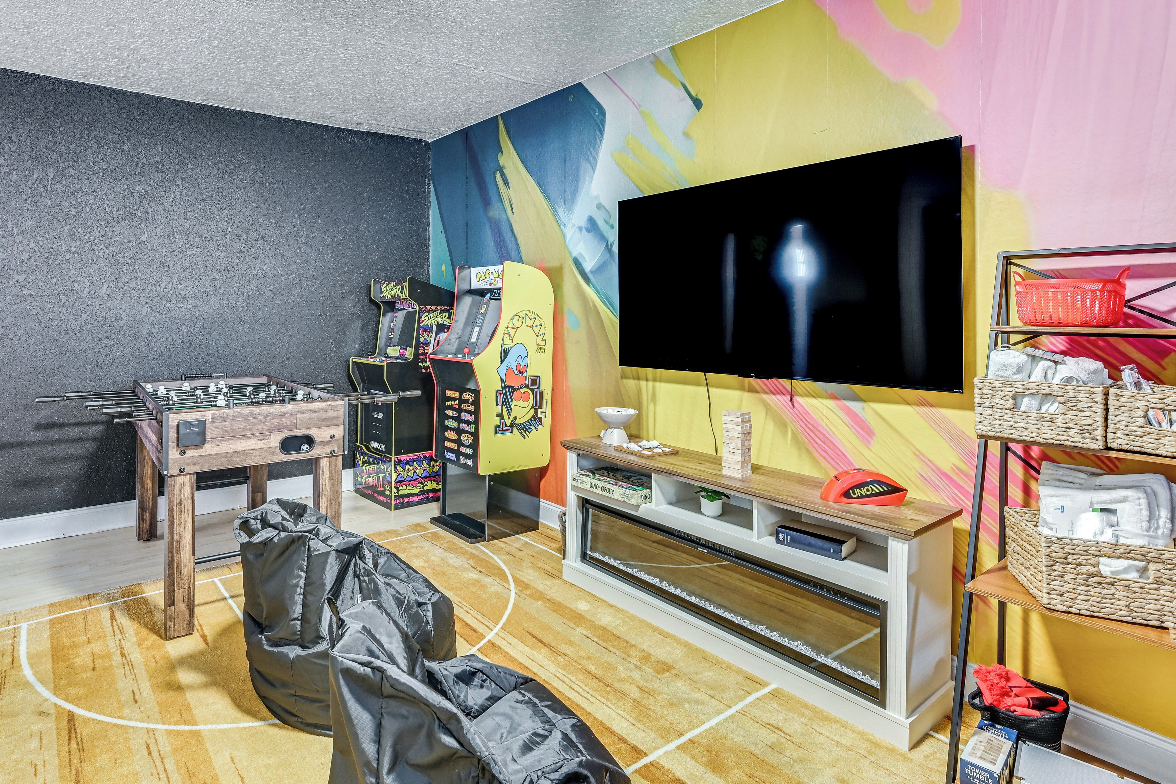 A room with a foosball table, a television, and a colorful mural.