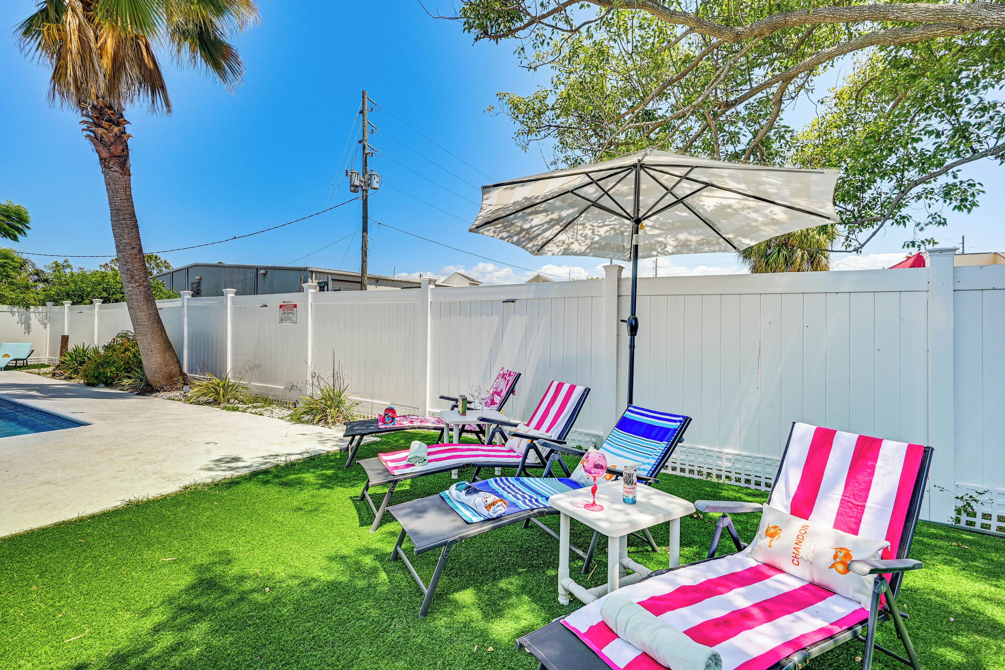 A backyard with a pool, lounge chairs, and an umbrella.