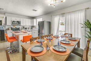 Una cocina moderna con armarios blancos, un refrigerador de acero inoxidable y una zona de comedor con sillas naranjas y una mesa de madera para seis personas.