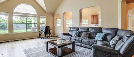 A spacious living room with a dark leather sofa, a glass-top coffee table, and a ceiling fan.