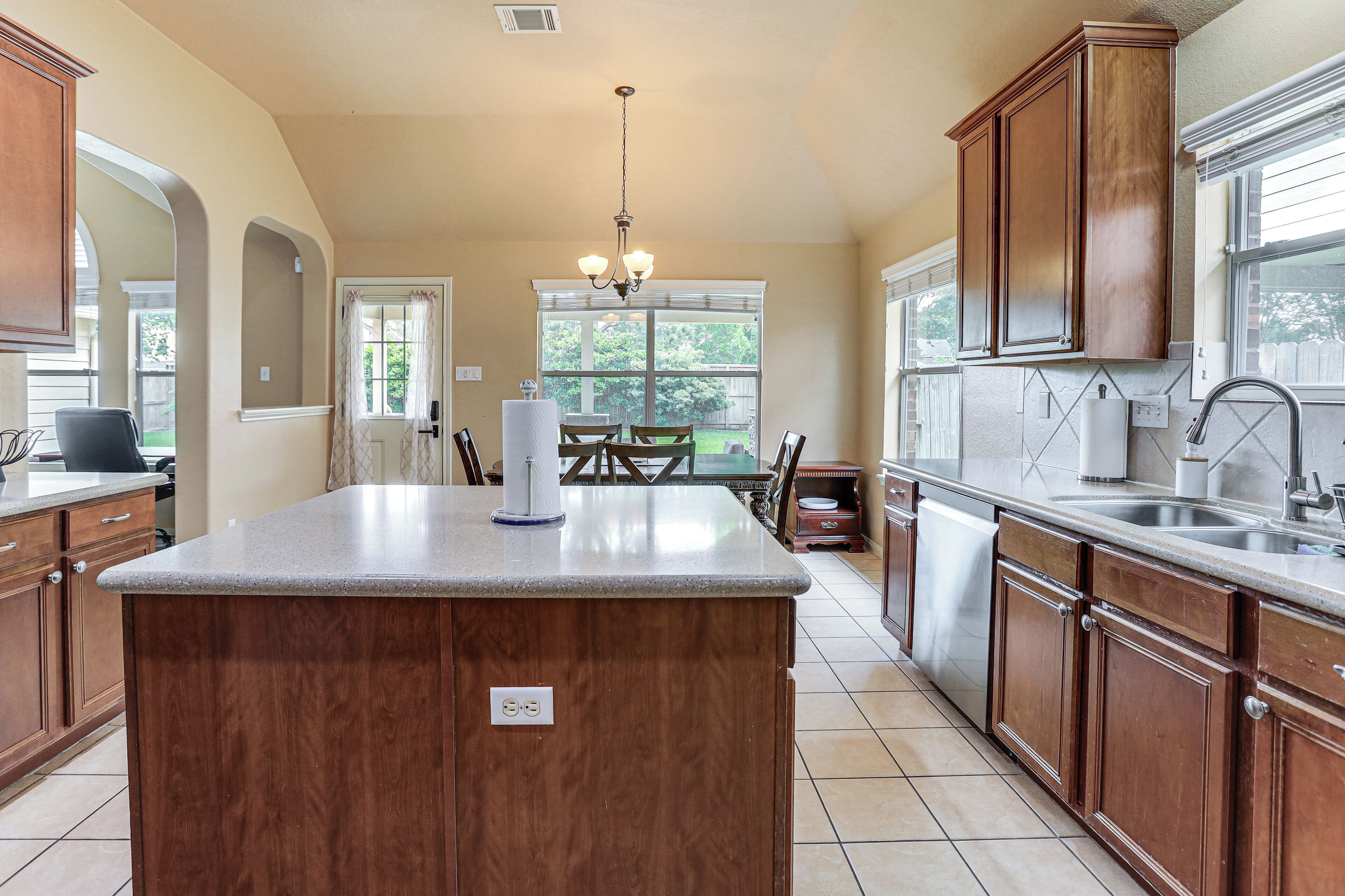 A kitchen with a central island, wooden cabinets, a chandelier, and a dining area with a table and chairs.