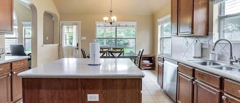 A kitchen with a central island, wooden cabinets, a chandelier, and a dining area with a table and chairs.