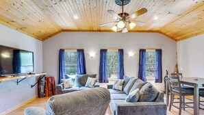 Ein Wohnzimmer mit Deckenventilator, Fernseher, Sofagarnitur und Esstisch.