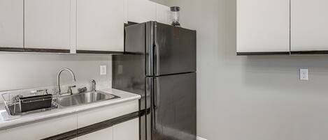 A kitchen with white cabinets, a stainless steel refrigerator, and a sink with a dish rack.