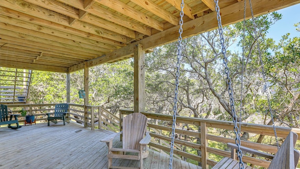 A wooden deck with a swing, chairs, and a view of trees. - < 1 Mi to Ocean! OBX Condo w/ Decks, Pets Welcome (Hatteras)