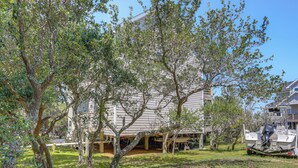 A house with a covered porch, a boat docked outside, and a tree in the foreground. - < 1 Mi to Ocean! OBX Condo w/ Decks, Pets Welcome (Hatteras)