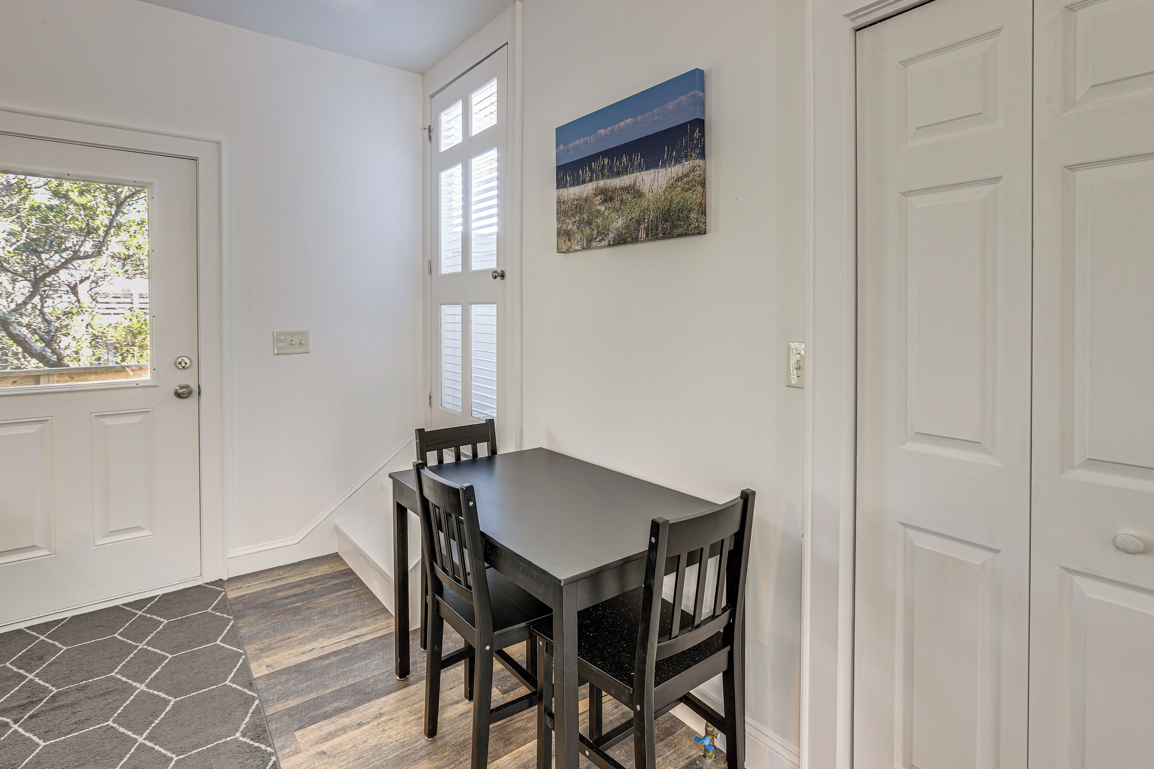 A dining area with a table and chairs, a door, and a wall-mounted picture.