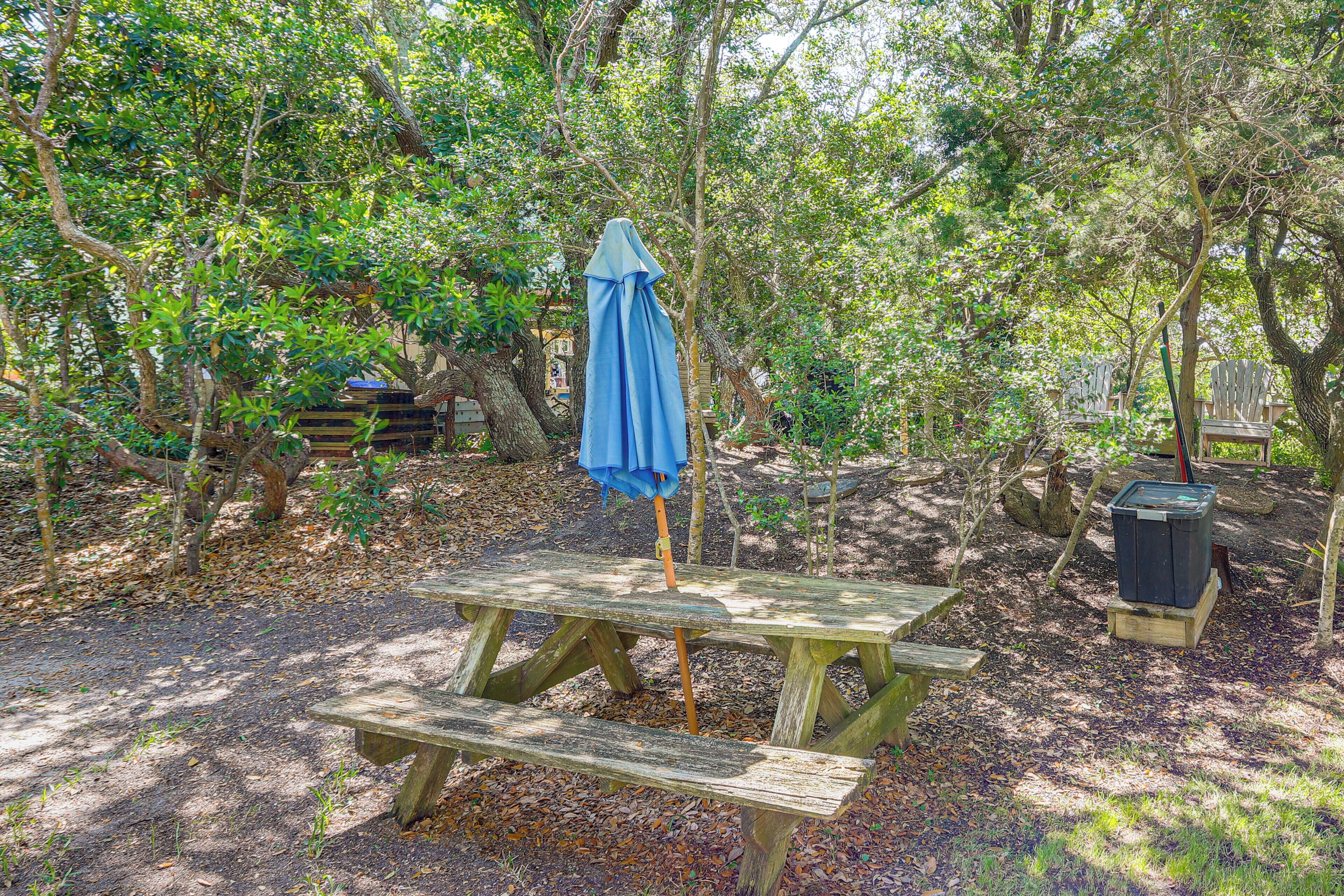 A wooden picnic table with a blue umbrella in a wooded area.