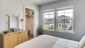 Ein Schlafzimmer mit Bett, Kommode, Spiegel und einem Fenster mit Blick auf ein Haus.