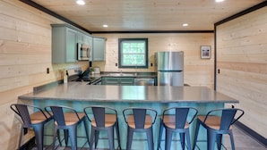 Una cocina con paredes de madera, una isla central con taburetes de bar, electrodomésticos de acero inoxidable y una ventana.
